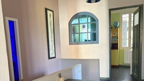 Quarto com escrivaninha escura, estantes com livros e brinquedos, uma moldura, um globo e uma janela com vista para o exterior.