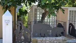 Escultura em metal de ursos em um pátio com parede de pedra e um pilar branco com uma placa.