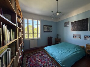 A bedroom with a bed, a bookshelf, a window, and a radiator.