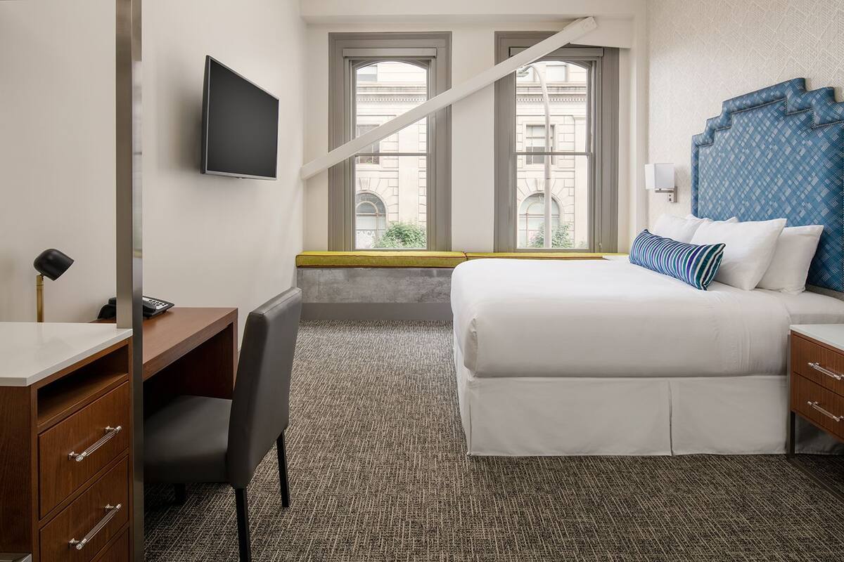 Una habitación de hotel con cama, escritorio, silla y televisor montado en la pared.