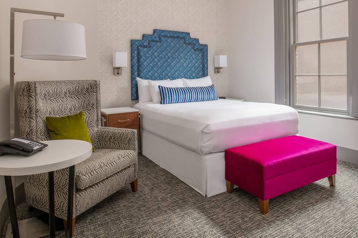 Una habitación de hotel con una cama, una silla, una mesita y una ventana.