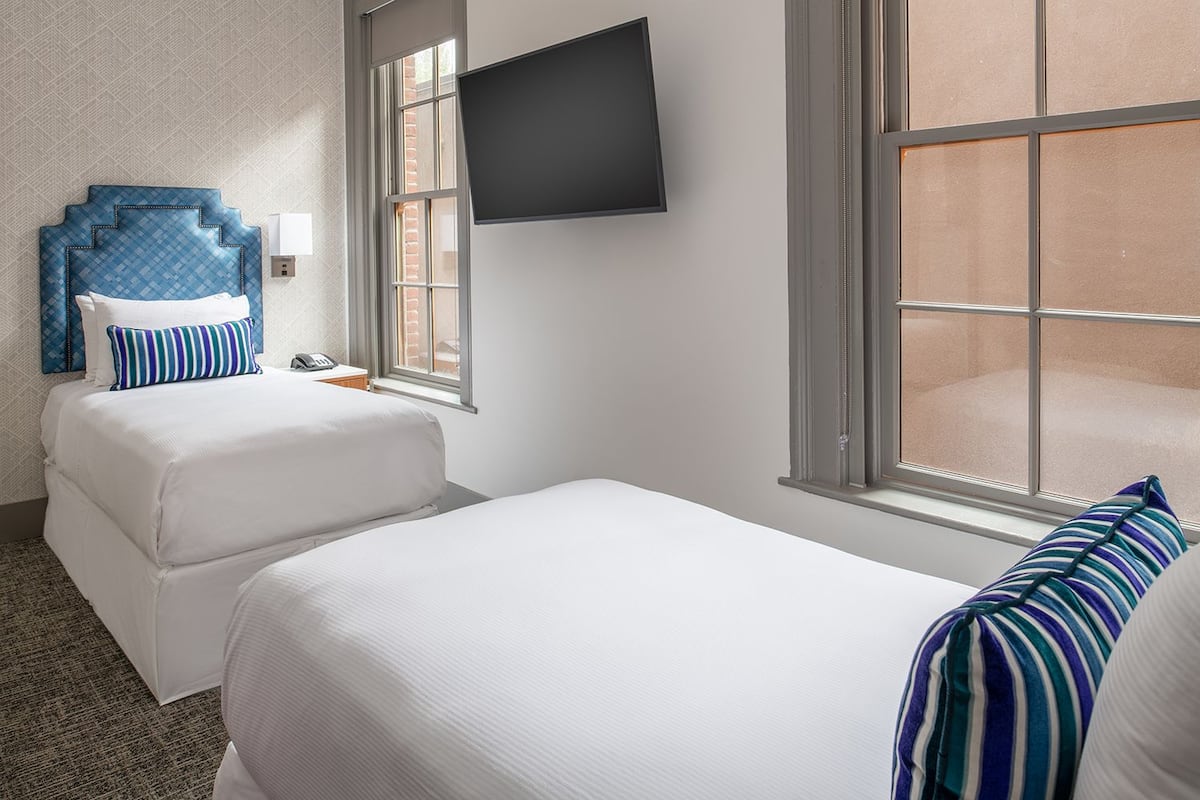 Habitación de hotel con dos camas, un televisor montado en la pared y ventana con vistas al exterior.