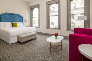 A hotel room with a bed, a bench, a small table with flowers, a chair, and large windows. - Harlow Hotel (Portland)