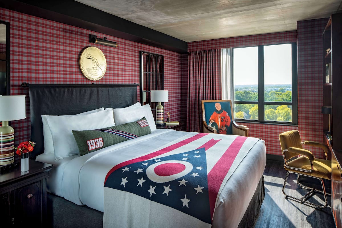 A hotel room with a large bed, a view of the city, and a painting on the wall.