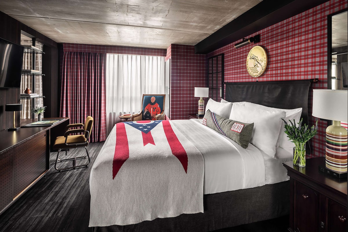 A hotel room with a large bed, a desk, a chair, a television, and a red plaid wall.