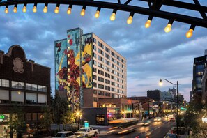 A multi-story building with a large mural on its facade, a street with vehicles, and a clear sky.