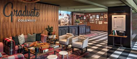 A hotel lobby with a checkered floor, a sofa set, armchairs, a coffee table, and a reception desk.