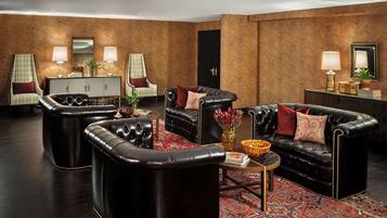 A spacious living room with a herringbone-patterned wall, a black leather sofa set, a matching armchair, a small side table, and a patterned rug.