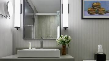 A modern bathroom with a large mirror, two wall-mounted lights, a sink, a toilet, and a framed picture on the wall.