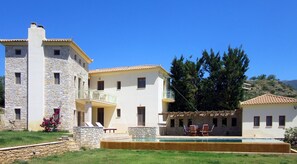 A two-story building with a stone facade, a balcony, and a swimming pool area with lounge chairs.
