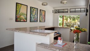 A modern kitchen with a granite countertop, a vase with flowers, and three framed paintings on the wall. - Hotel Patio Grande (Flores)