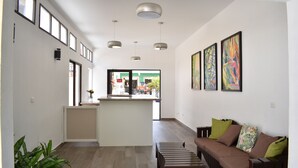 A spacious living area with a sofa, a coffee table, and a kitchen island. There are pendant lights and framed artwork on the walls. - Hotel Patio Grande (Flores)