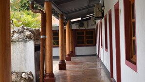 A covered corridor with wooden columns, a tiled floor, and a stone wall with a rock formation. - Hotel Patio Grande (Flores)
