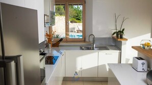 Una cocina moderna con horno empotrado, un lavamanos y ventana con vistas a una piscina.