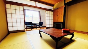A tatami mat room with a low table, two chairs, a sliding door, and a view of the outdoors.