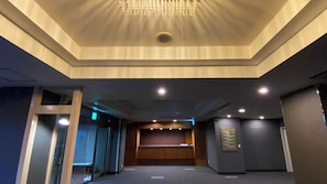 A hotel lobby with a chandelier, recessed lighting, a reception desk, and a framed artwork on the wall.