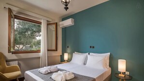 A hotel room with a bed, a chair, a window with curtains, an air conditioner, and bedside lamps. - Villa 15  Elegant Private Pool Family (Rethymno)