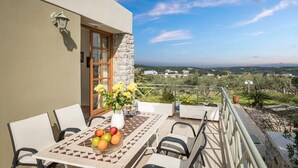 A balcony with a table set for dining, a vase of flowers, and a view of the countryside. - Villa 15  Elegant Private Pool Family (Rethymno)