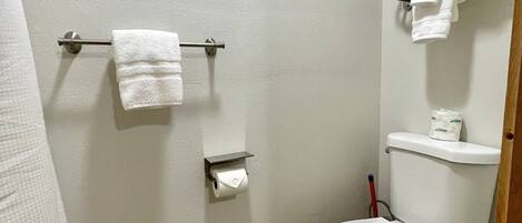 Une petite salle de bain propre, équipée de toilettes, d’un porte-serviettes et d’un support à papier toilette.