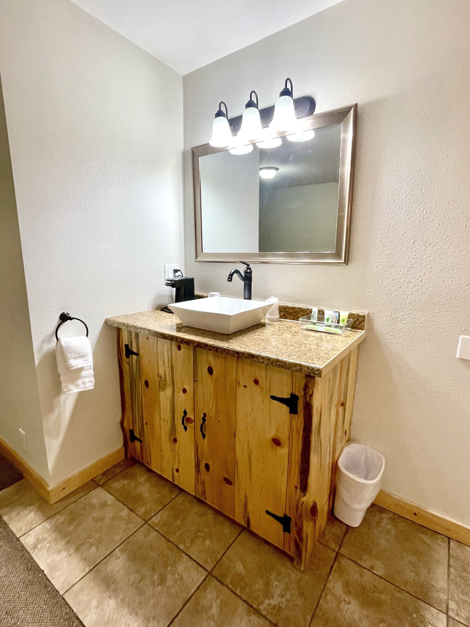 A bathroom with a wooden vanity, a white sink, and a mirror with three lights.