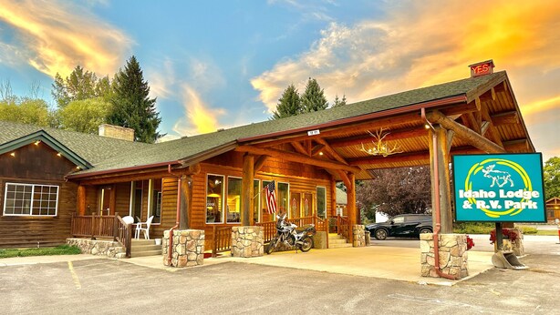 A lodge with a covered porch, stone pillars, and an American flag. - Idaho Lodge and RV Park (Bonners Ferry)