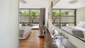A modern hotel room with a large bed, a sitting area with a bench, a glass shower, and a view of the outdoors. - Villa 7 Masterwork Contemporary (Chania)