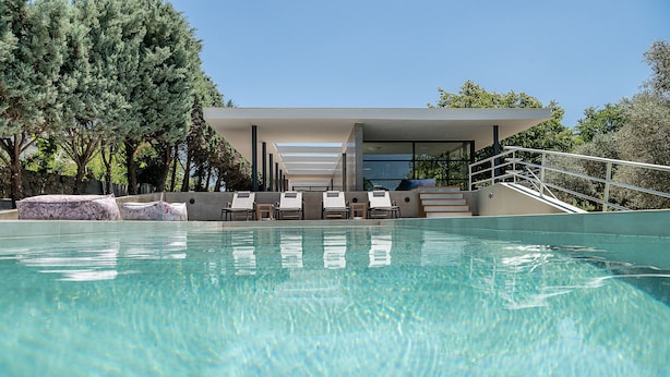 A swimming pool with lounge chairs and a modern building with a glass facade. - Villa 7 Masterwork Contemporary (Chania)
