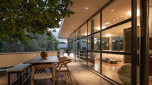 An outdoor patio with a wooden table and chairs, a stone sculpture, and a glass wall offering a view of the interior. - Villa 7 Masterwork Contemporary (Chania)