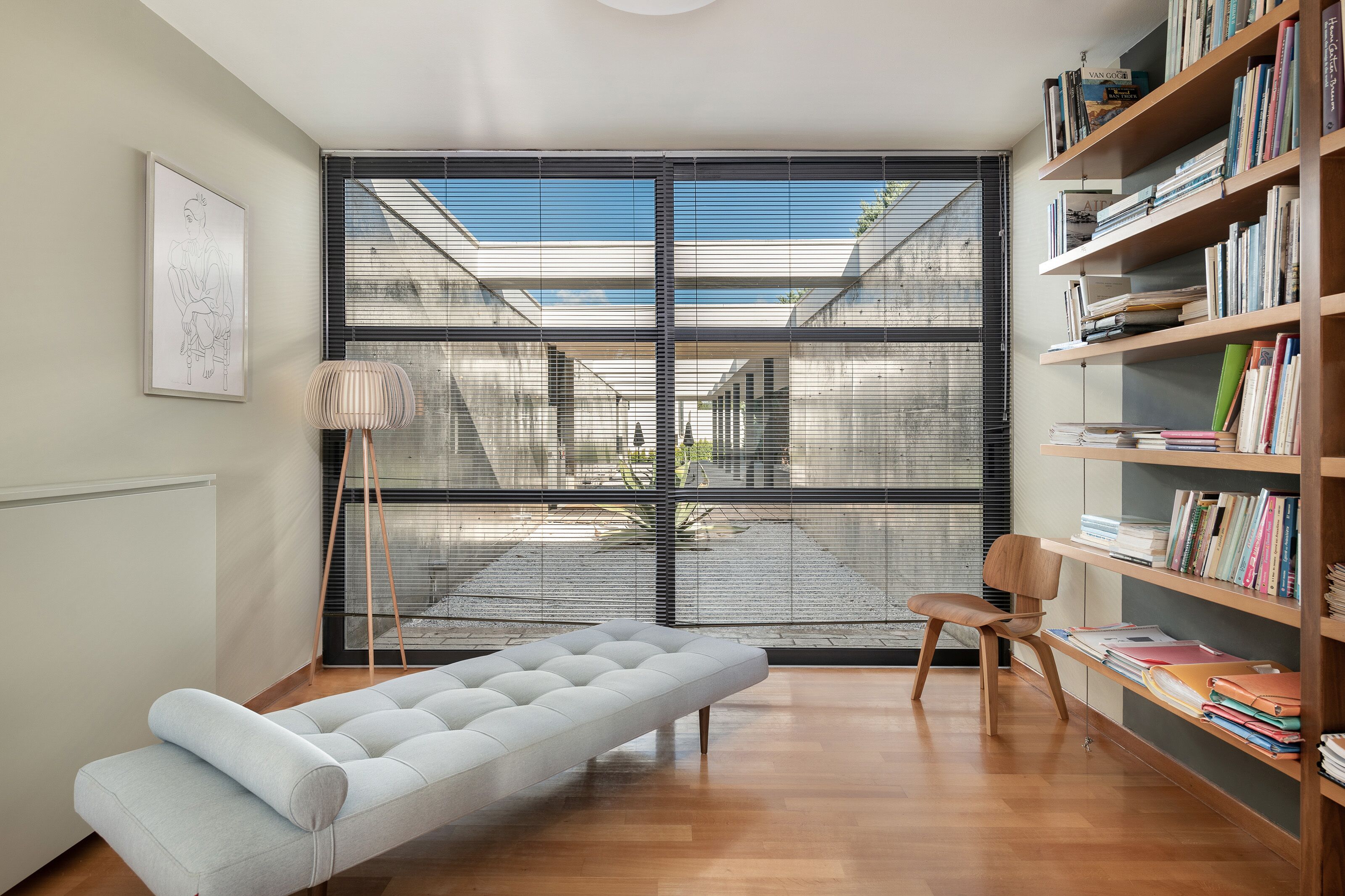 Una habitació moderna amb un finestral gran, un sofà, una cadira i una biblioteca.