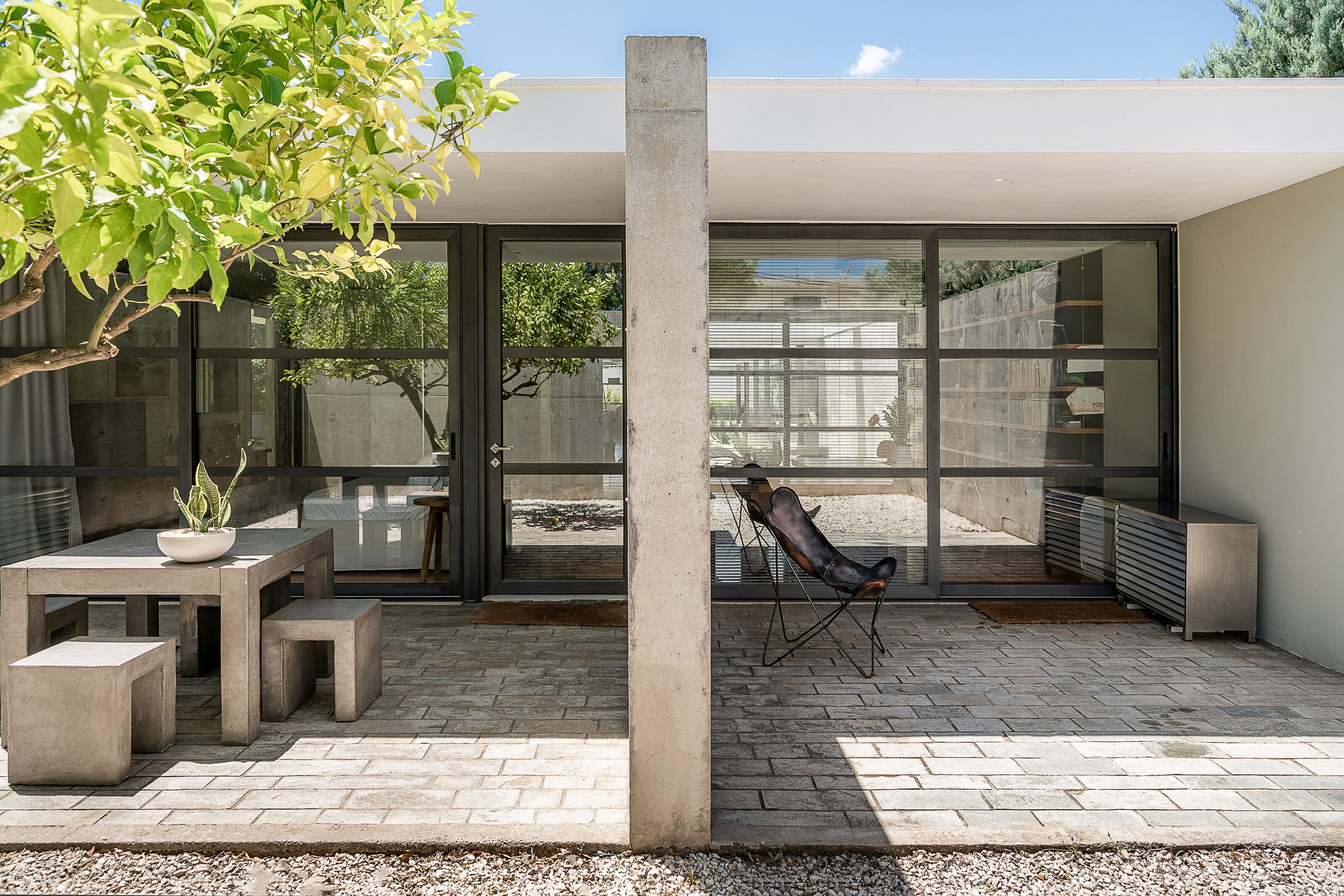 A patio with a concrete table and benches, a potted plant, and a leather chair.