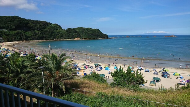 A beach with umbrellas, people, and a view of the sea and hills. - Sokai No Yado Narainokaze (Shimoda)