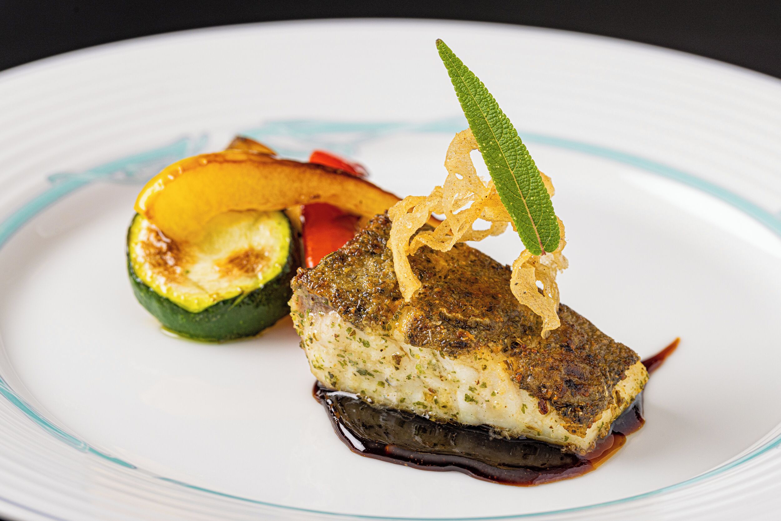 Une assiette contenant un morceau de poisson, une tranche de courgette et une garniture.