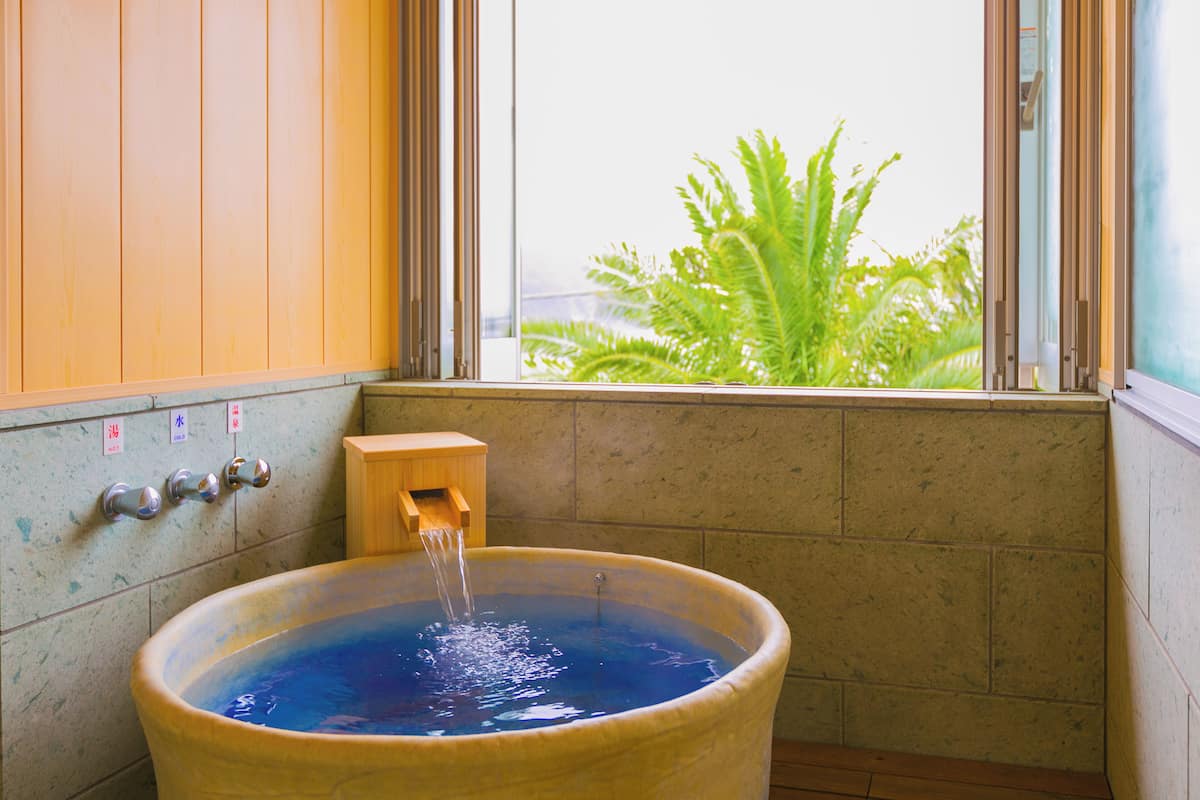 A bathtub with water running, a wooden cabinet, and a window with a view of greenery.