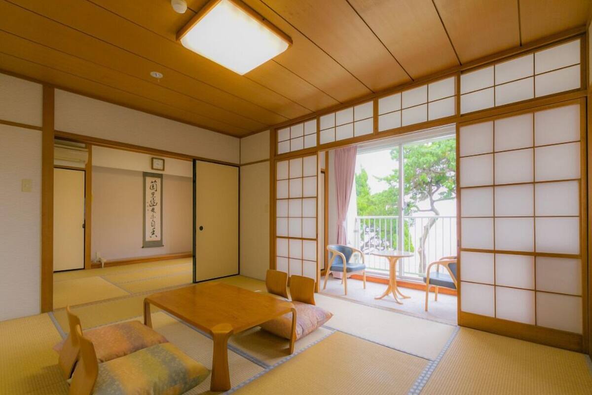 Um quarto japonês tradicional com piso de tatame, uma mesa de madeira baixa e portas deslizantes que dão para uma varanda.