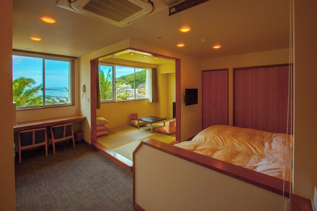 A hotel room with a bed, a desk, a chair, and a view of the ocean.