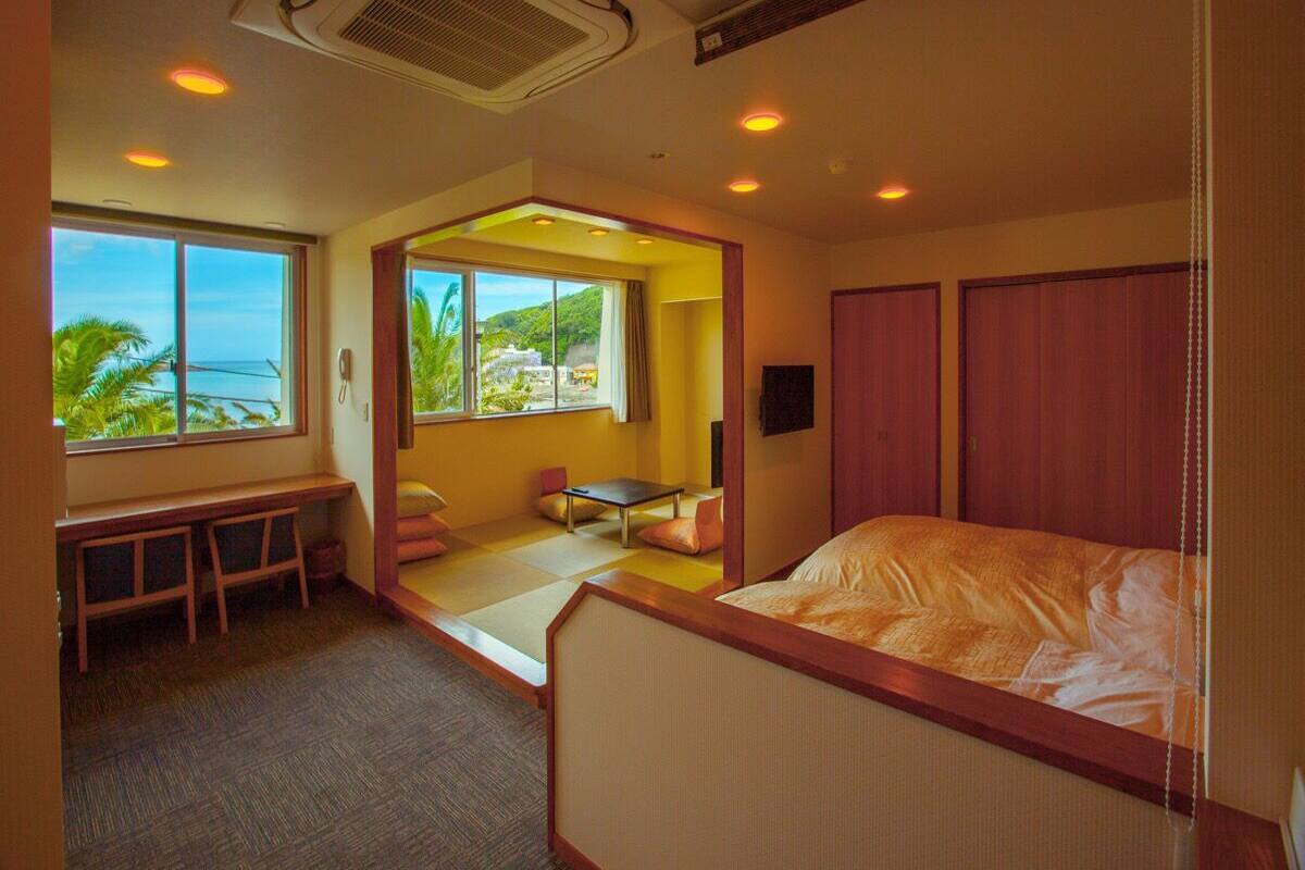 Quarto de hotel com cama, escrivaninha, cadeira, mesa pequena e vista para o exterior.