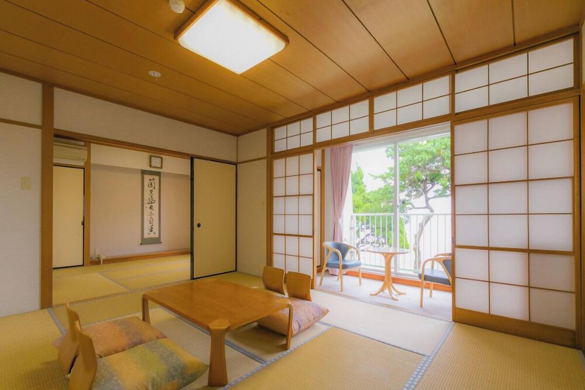 Um quarto japonês tradicional com tatames, uma mesa de madeira baixa e portas deslizantes que dão para uma varanda externa.