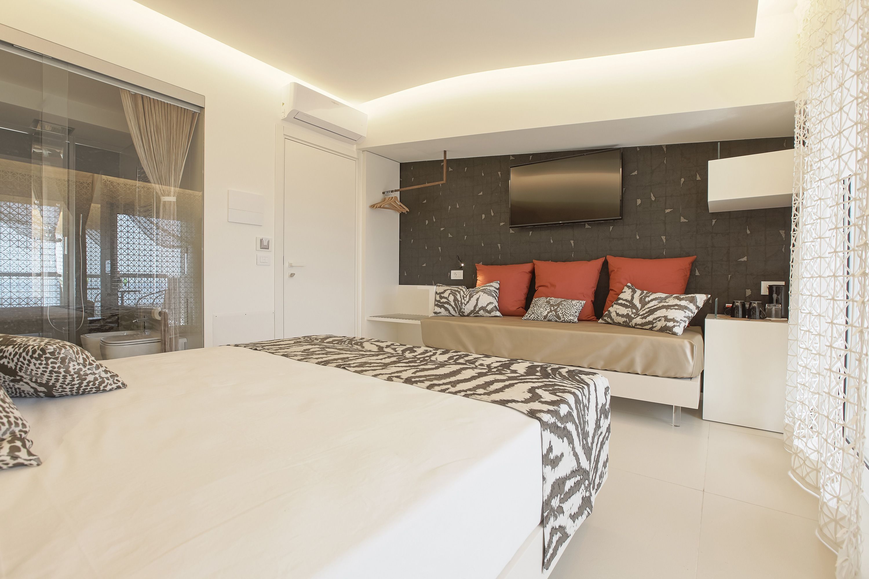 Quarto moderno com uma cama grande, sofá-cama, TV de tela plana na parede e porta de vidro que dá para uma varanda.