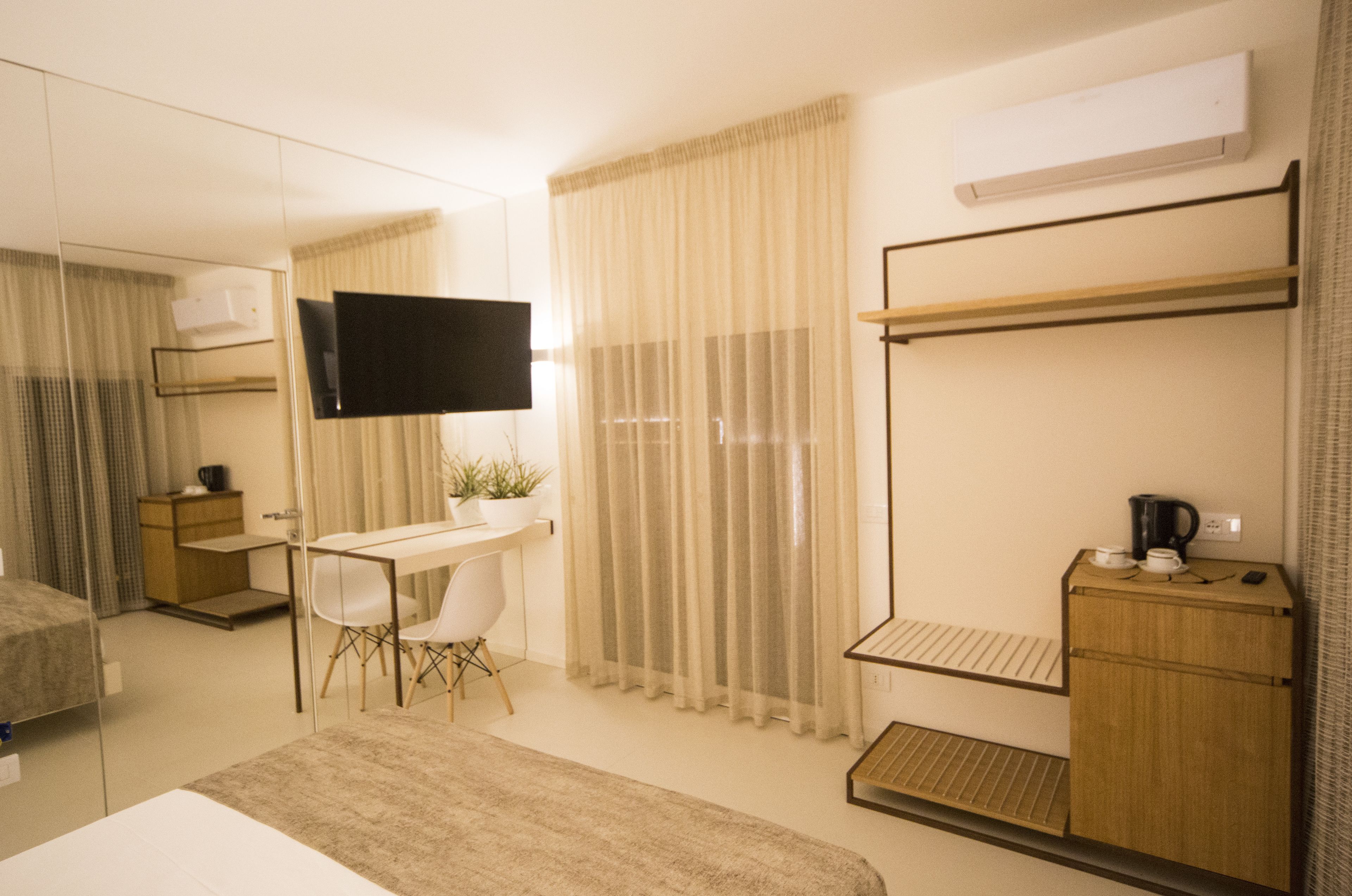 Habitación de hotel con cama, escritorio, silla, televisor, armario y ventana con cortinas.
