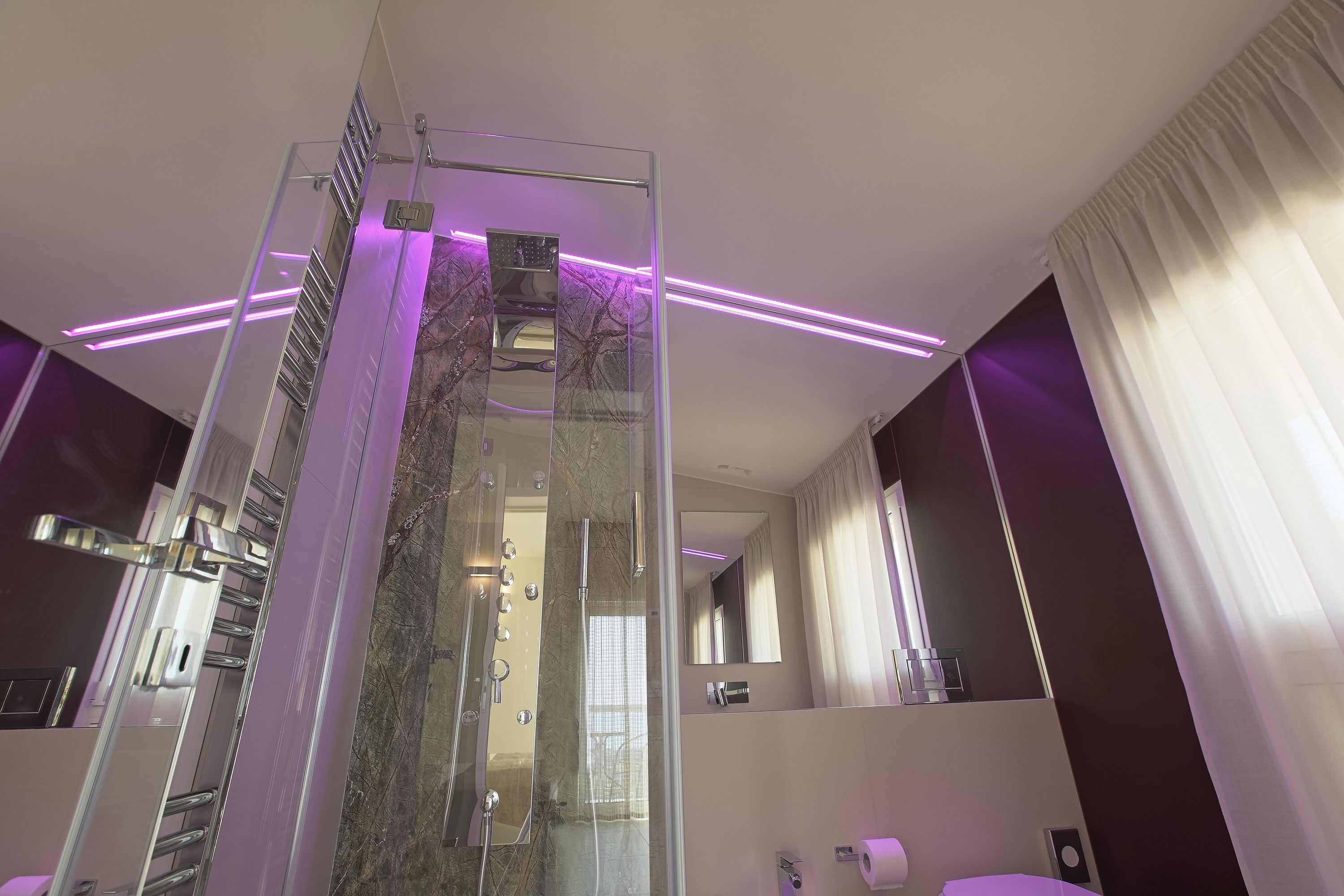 Un baño moderno con cabina de ducha de vidrio, tocador con espejo e iluminación ambiental morada.