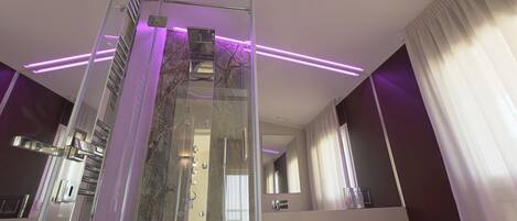 Un baño moderno con cabina de ducha de vidrio, tocador con espejo e iluminación ambiental morada.