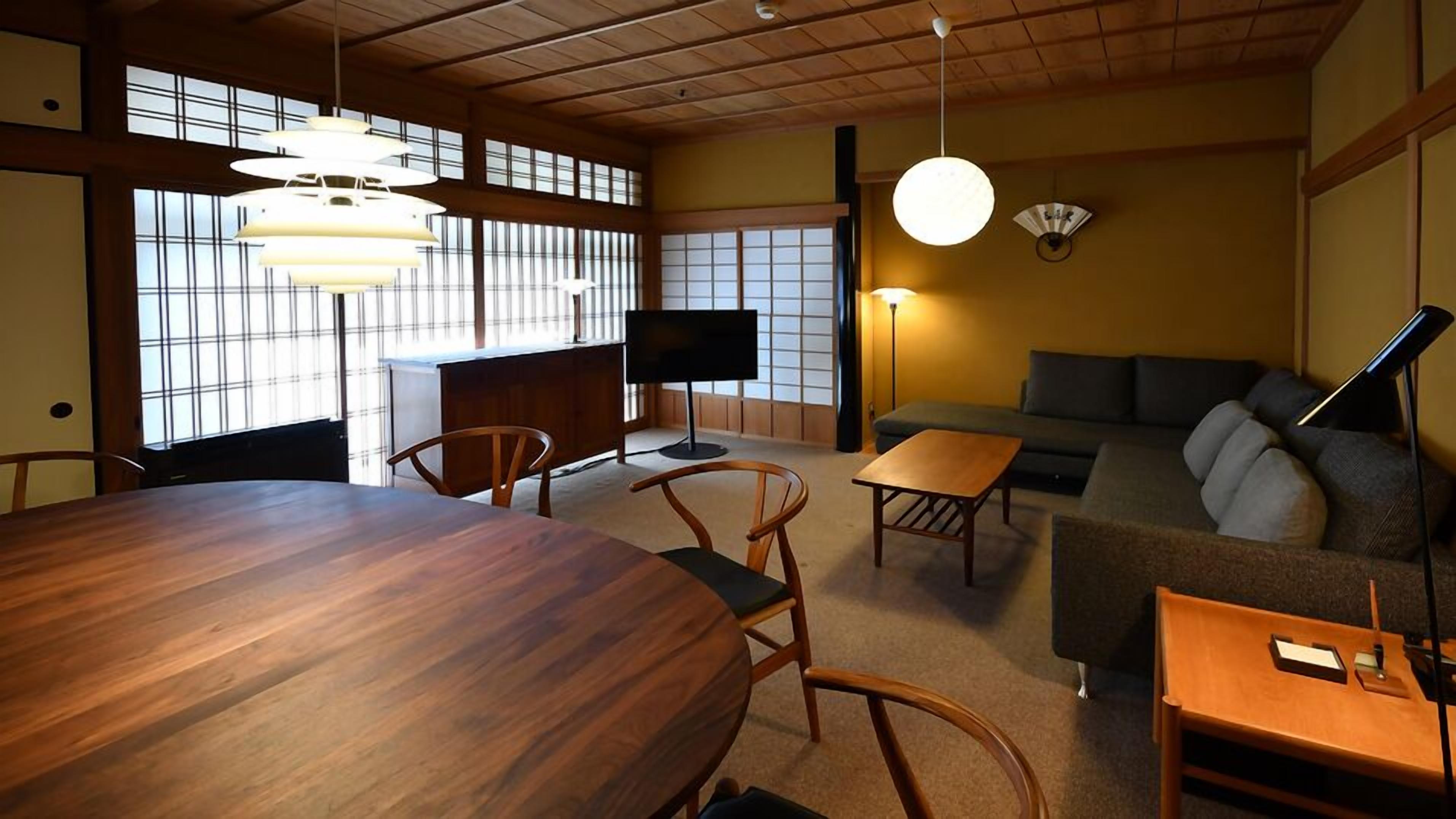 Une pièce de style japonais traditionnel, avec un sol recouvert de tatamis, une table basse, un canapé et un téléviseur.