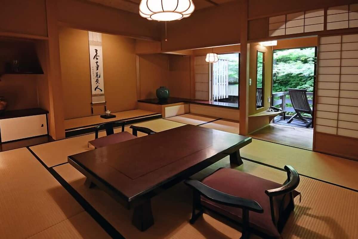 A traditional Japanese room with tatami flooring, a low table, and a sliding door leading to an outdoor area.