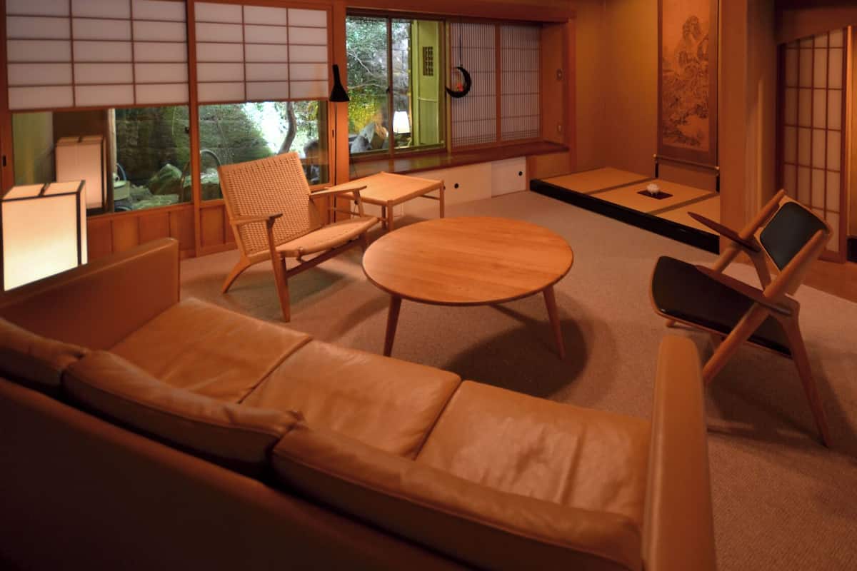 Ein traditioneller japanischer Raum mit Tatami-Boden, einem niedrigen Tisch, einer Couch und einem Sessel.
