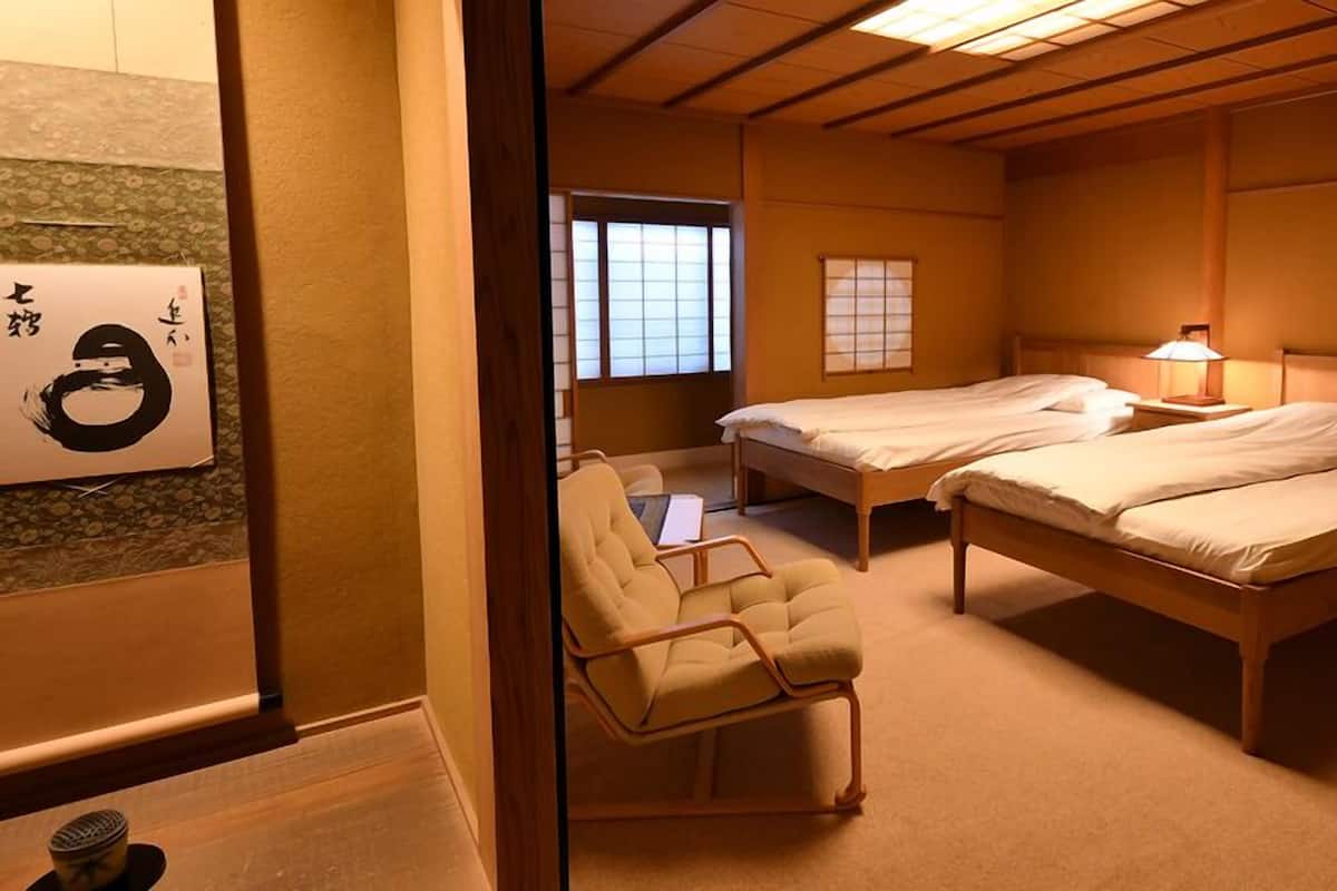 Ein traditionell gestalteter japanischer Raum mit zwei Einzelbetten, einem Holztisch und einem Stuhl aus Tatami-Matte.