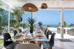 A dining area with a glass table, black chairs, and a view of the sea. - Very Coast Villa Romántica-Private pool 4 bedrooms, BBQ, wifi, Sea & Puerto View (Los Realejos,)