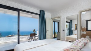 Un dormitorio con una cama grande, vistas al mar y un balcón con una silla.