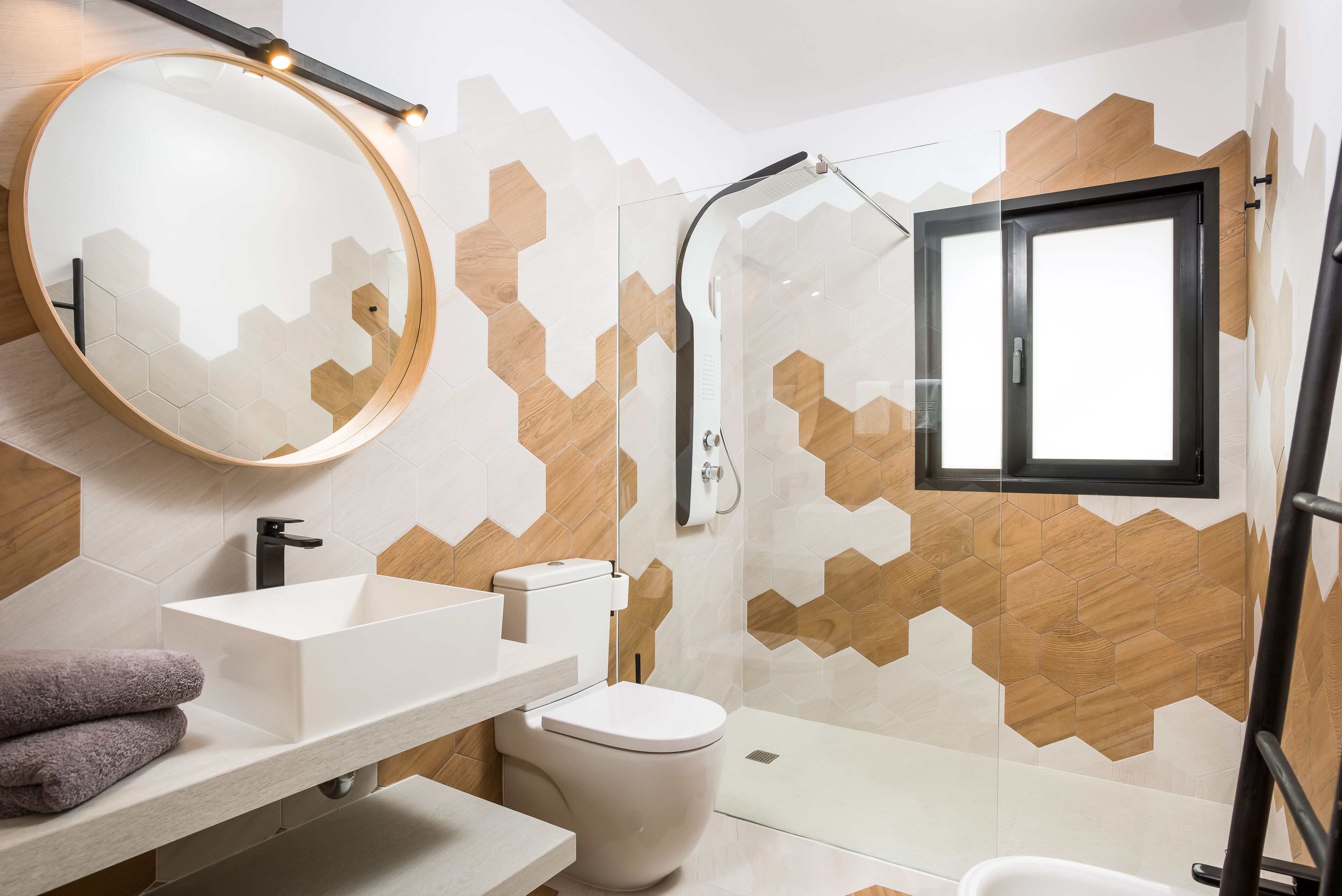 A modern bathroom with a round mirror, a white sink, a toilet, and a glass-enclosed shower.