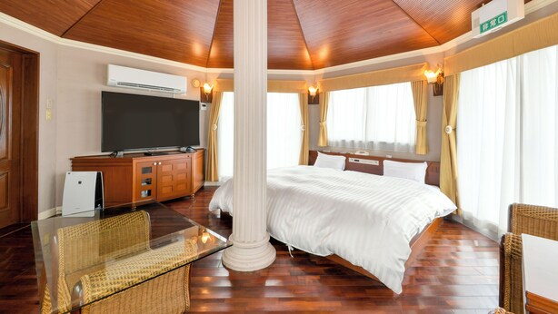 A hotel room with a large bed, a flat-screen TV, a glass coffee table, wicker furniture, and a wooden ceiling. - Hotel Castle inn Tsu (Tsu)