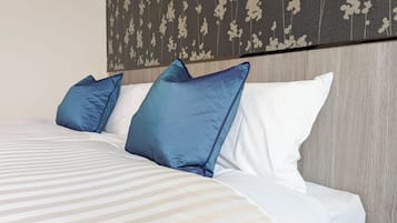 A neatly made bed with white and light grey striped bedding, two blue pillows, and a wooden headboard with a floral pattern.